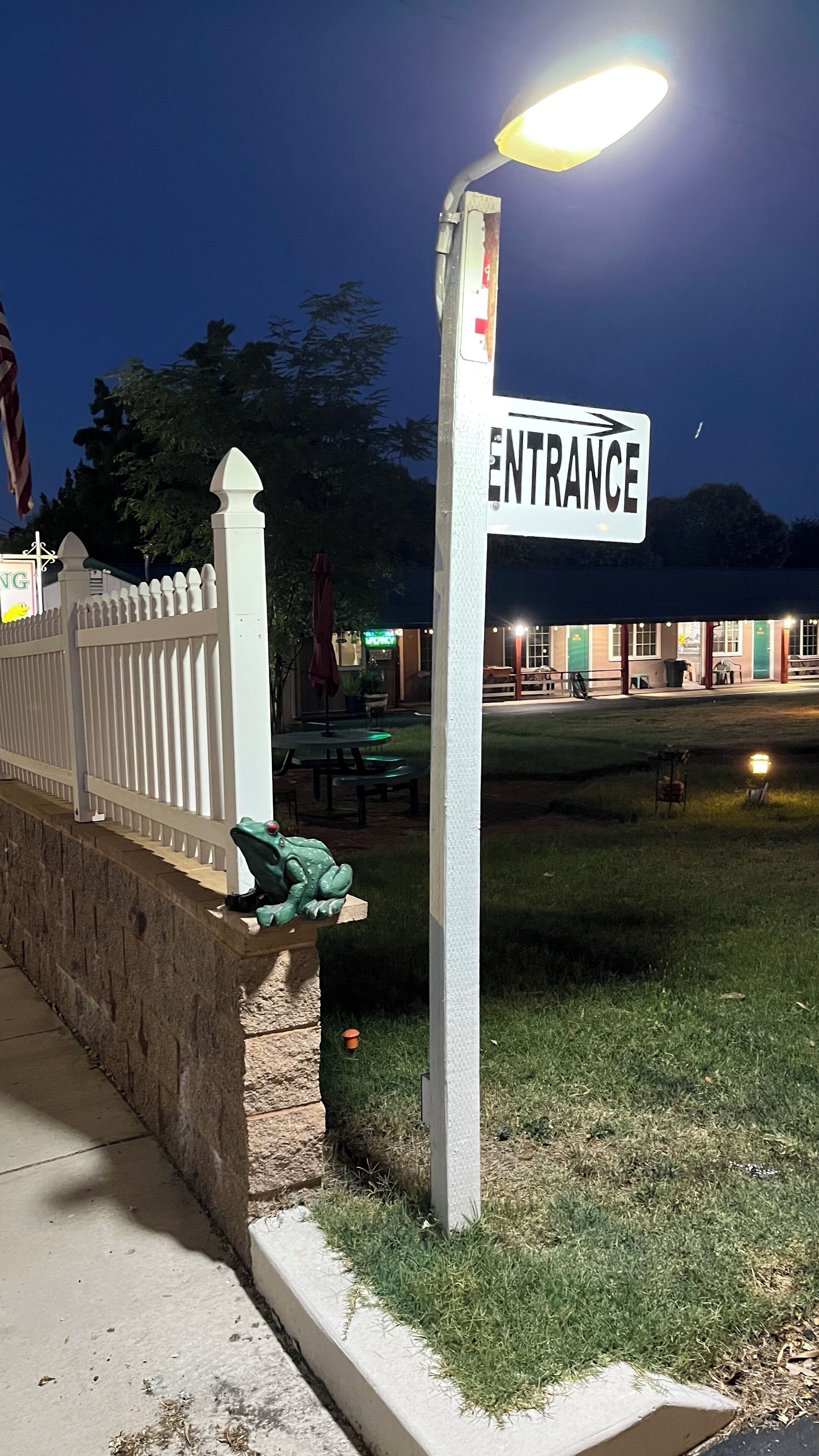 A white entrance sign with an arrow pointing right, a street lamp, and a white picket fence.
