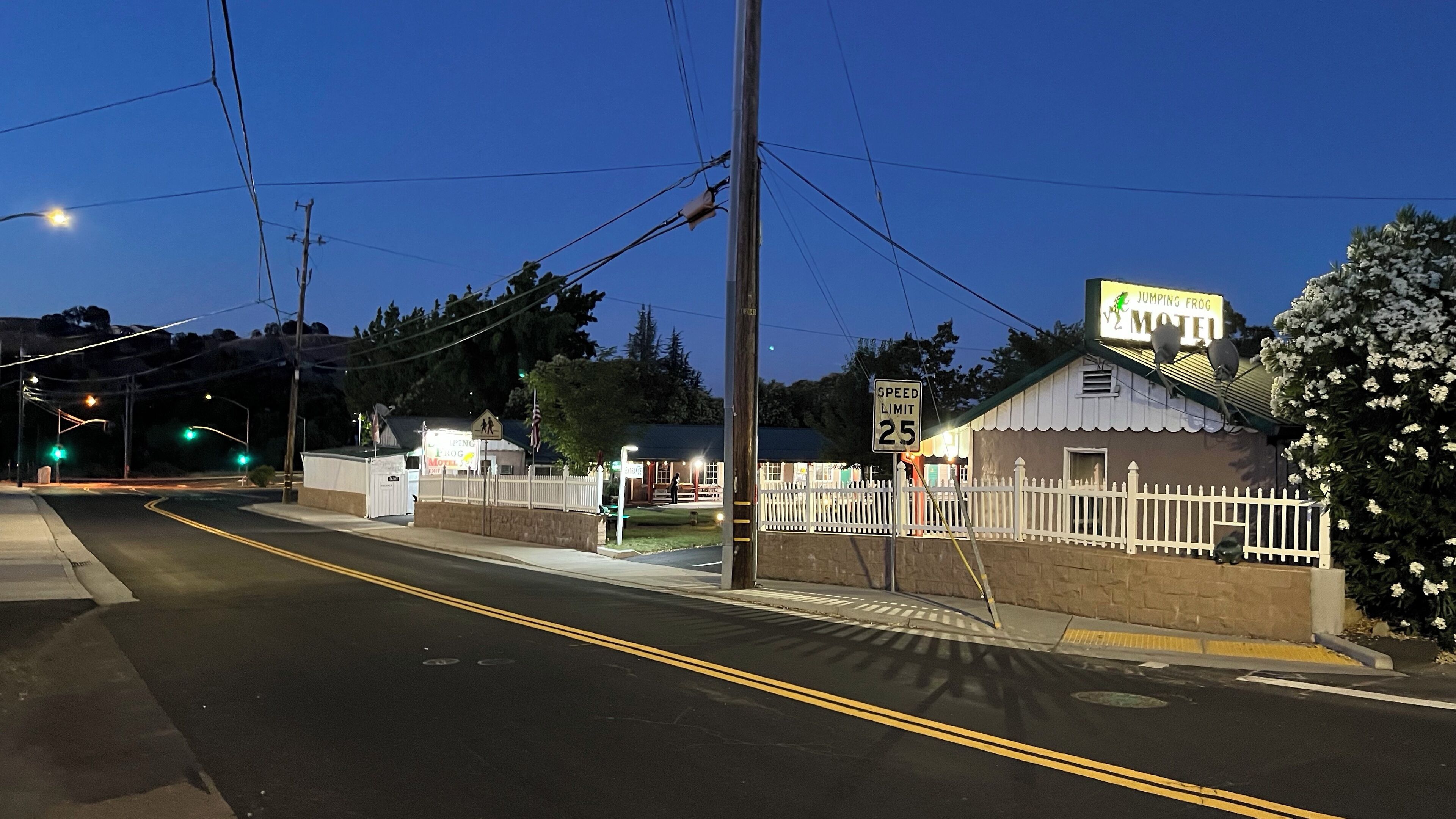 A motel with a speed limit sign of 25 mph, a pedestrian crossing, and a white picket fence.