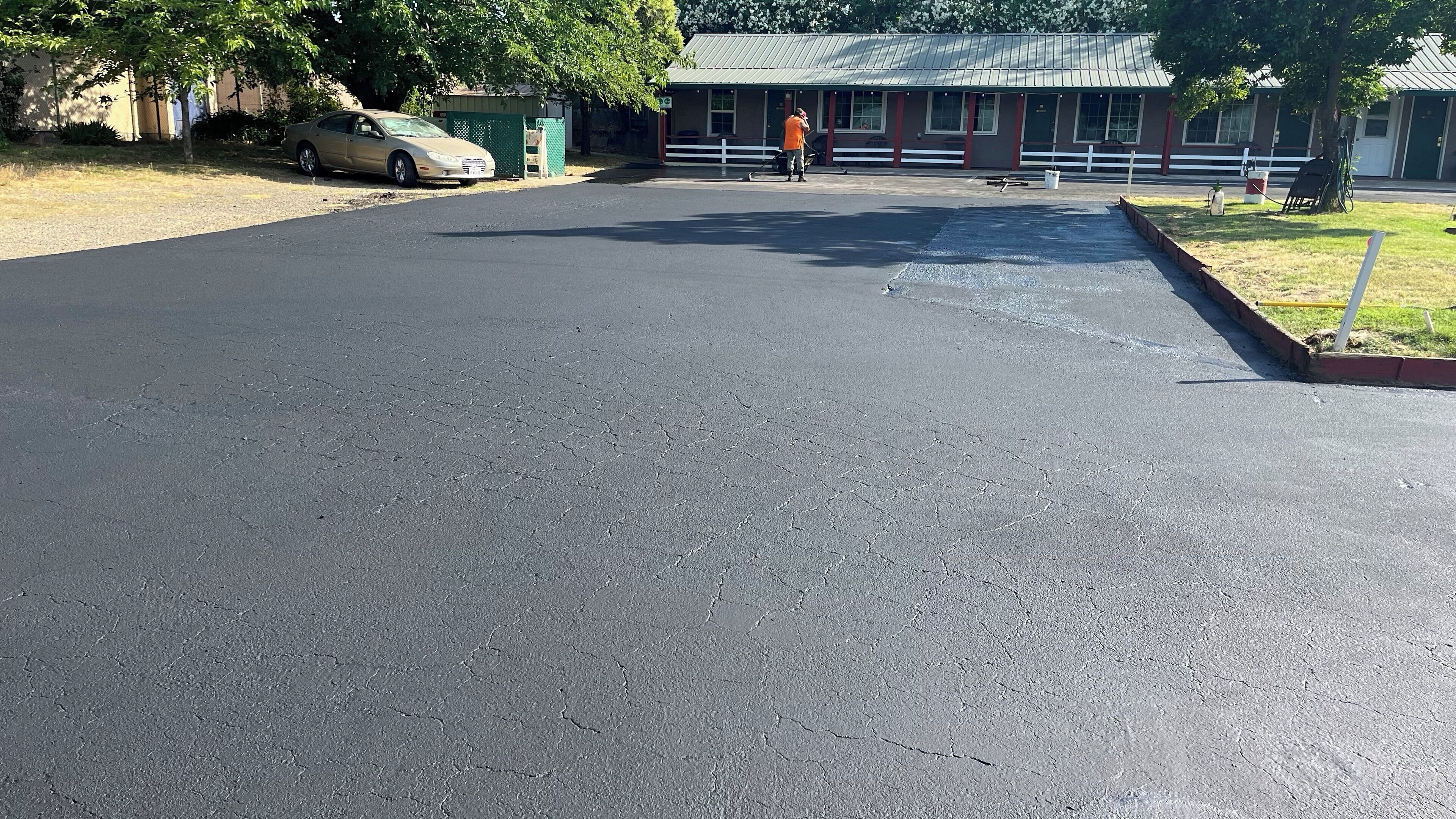 Ein gepflasterter Parkplatz mit einem Auto und einer Person in einem orangefarbenen Hemd.
