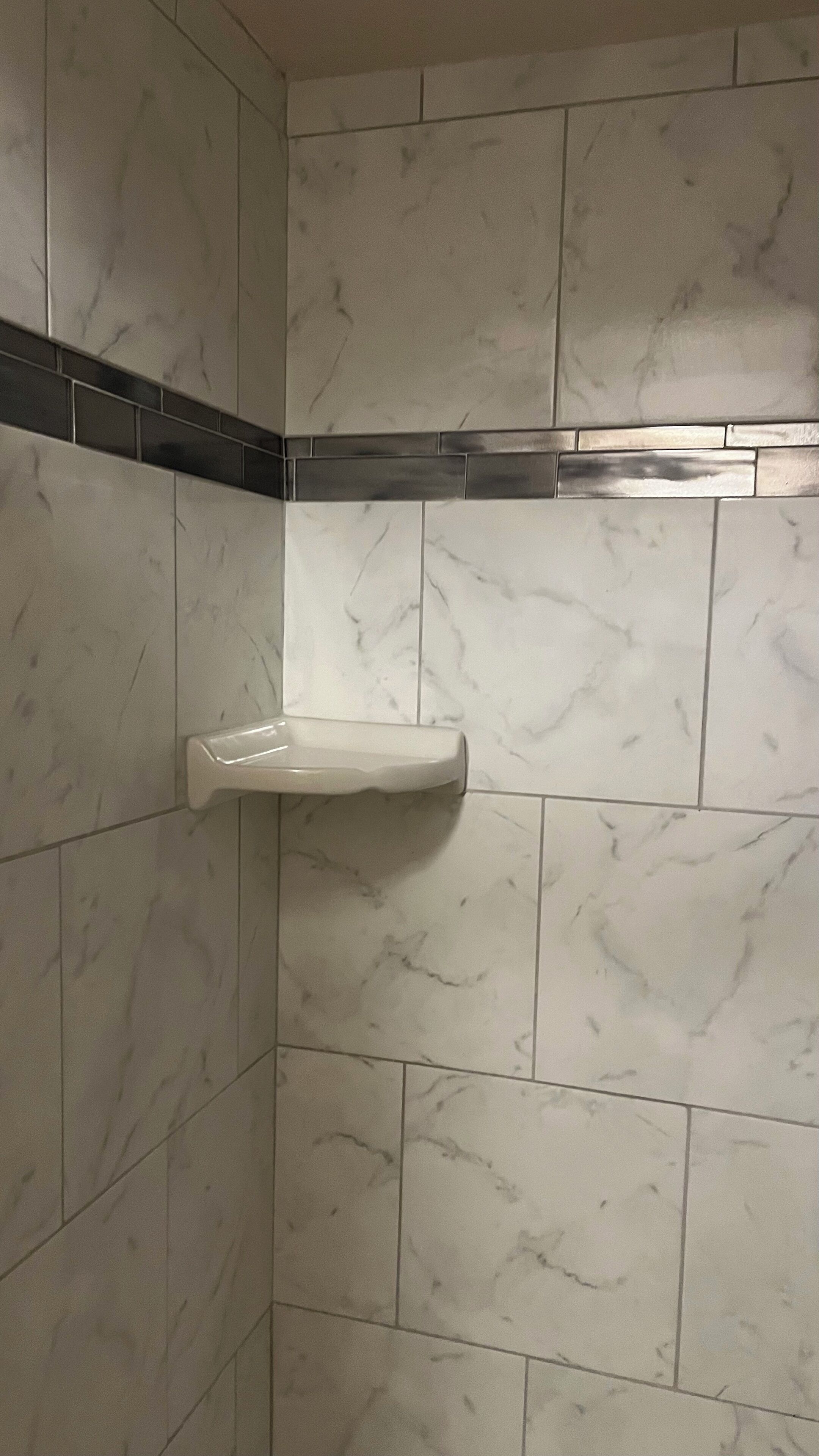 A bathroom with white marble tiles and a black and silver tile accent strip.