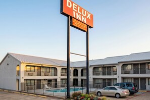 A hotel with a sign reading 'Delux Inn,' a pool, and a parking area.