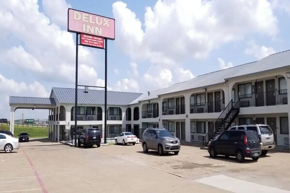 A DELUX INN hotel with a parking lot, multiple vehicles, and a clear sky.