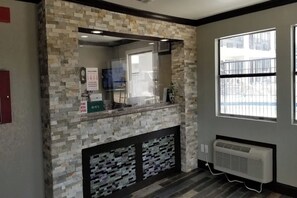 Zona de recepción con pared de piedra, separador de vidrio, televisor montado y ventana con vista a un edificio.