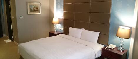 Une chambre d’hôtel avec un grand lit, deux tables de chevet, une commode, une lampe, un tableau et un téléphone.