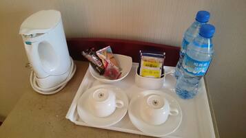 Un plateau contenant une cafetière, deux tasses à thé, un bol rempli de portions de nourriture emballées et une bouteille d’eau.
