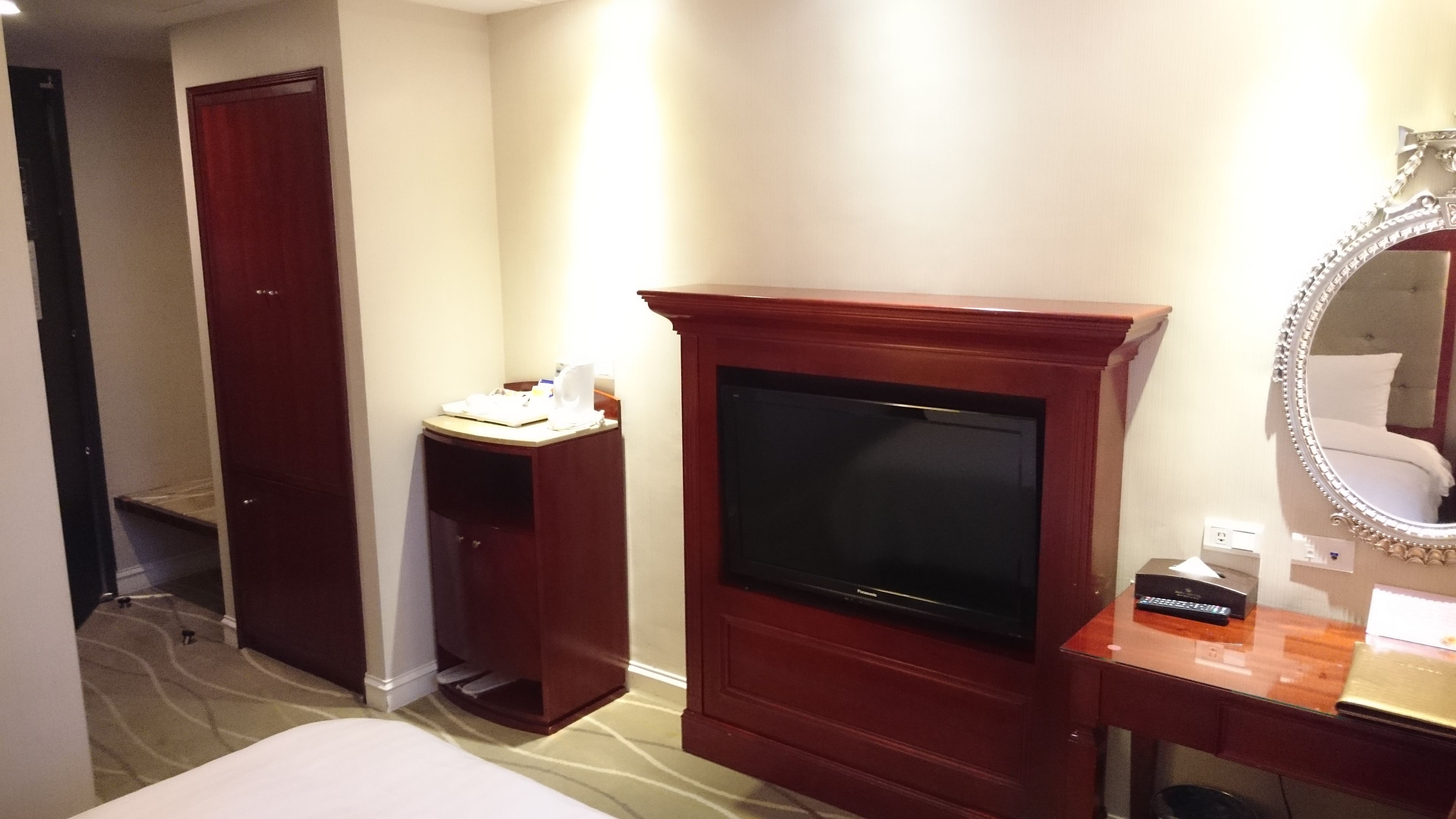 Una habitación de hotel con cama, televisión, tocador con espejo y escritorio.