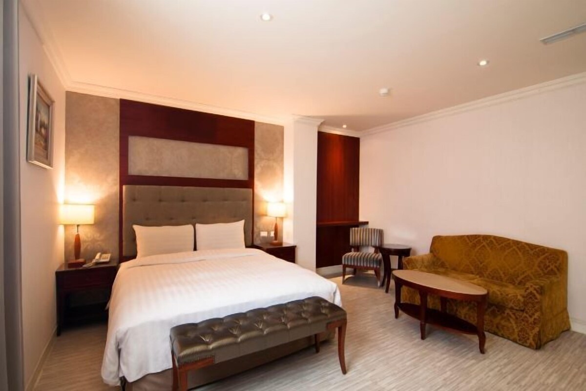 A hotel room with a large bed, a bench, a sofa, a chair, and a small table.