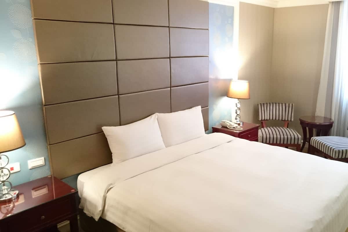 A hotel room with a large bed, a nightstand, a lamp, a chair, and a window with curtains.