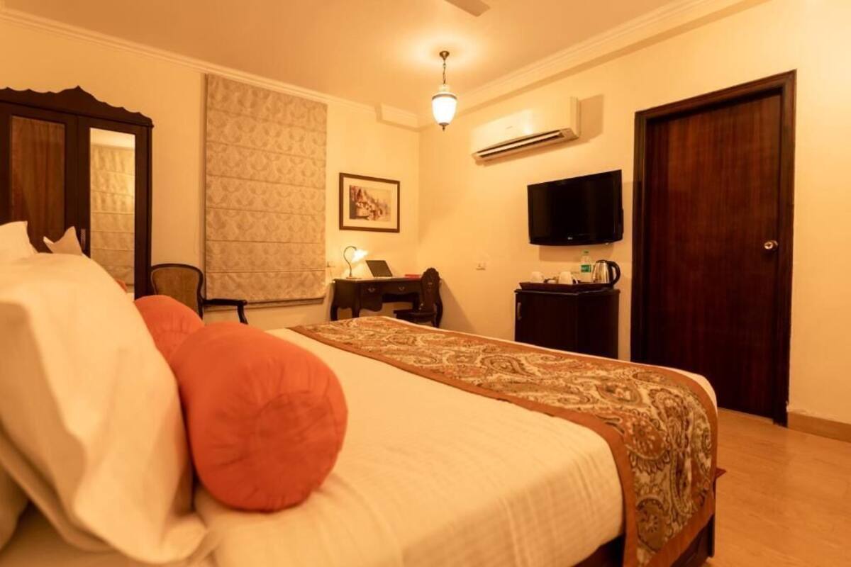 A hotel room with a bed, a desk with a laptop, a television, and an air conditioning unit.