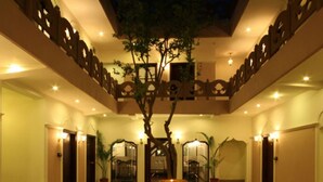 A courtyard with a central fountain, surrounded by chairs and potted plants, with a warm, inviting atmosphere. - Amritara Suryauday Haveli (Varanasi)