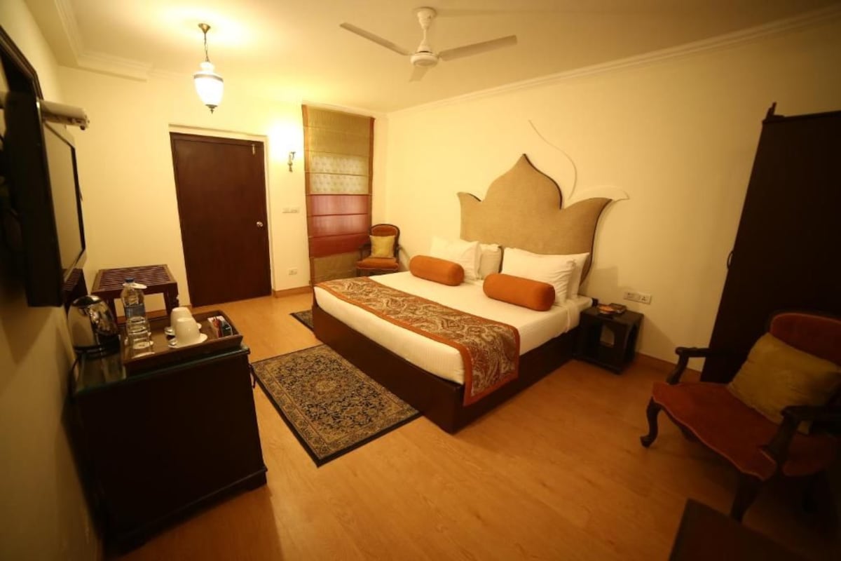 A bedroom with a bed, bedside tables, a desk, a chair, a ceiling fan, and a door.