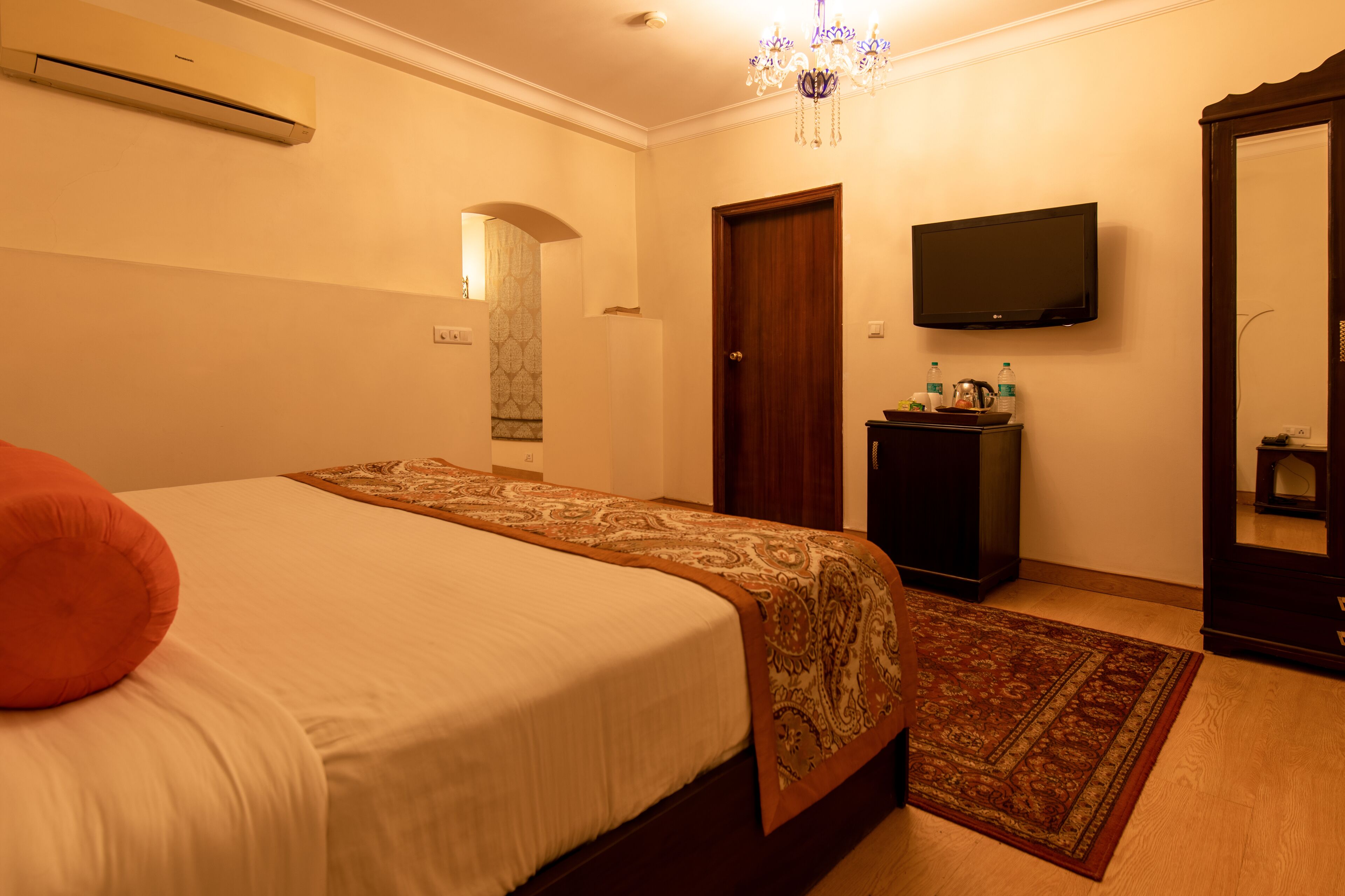A hotel room with a bed, a television, a wardrobe, and a mirror.