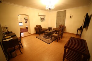 A living room with a wooden floor, a coffee table, two sofas, a chandelier, and a TV mounted on the wall.