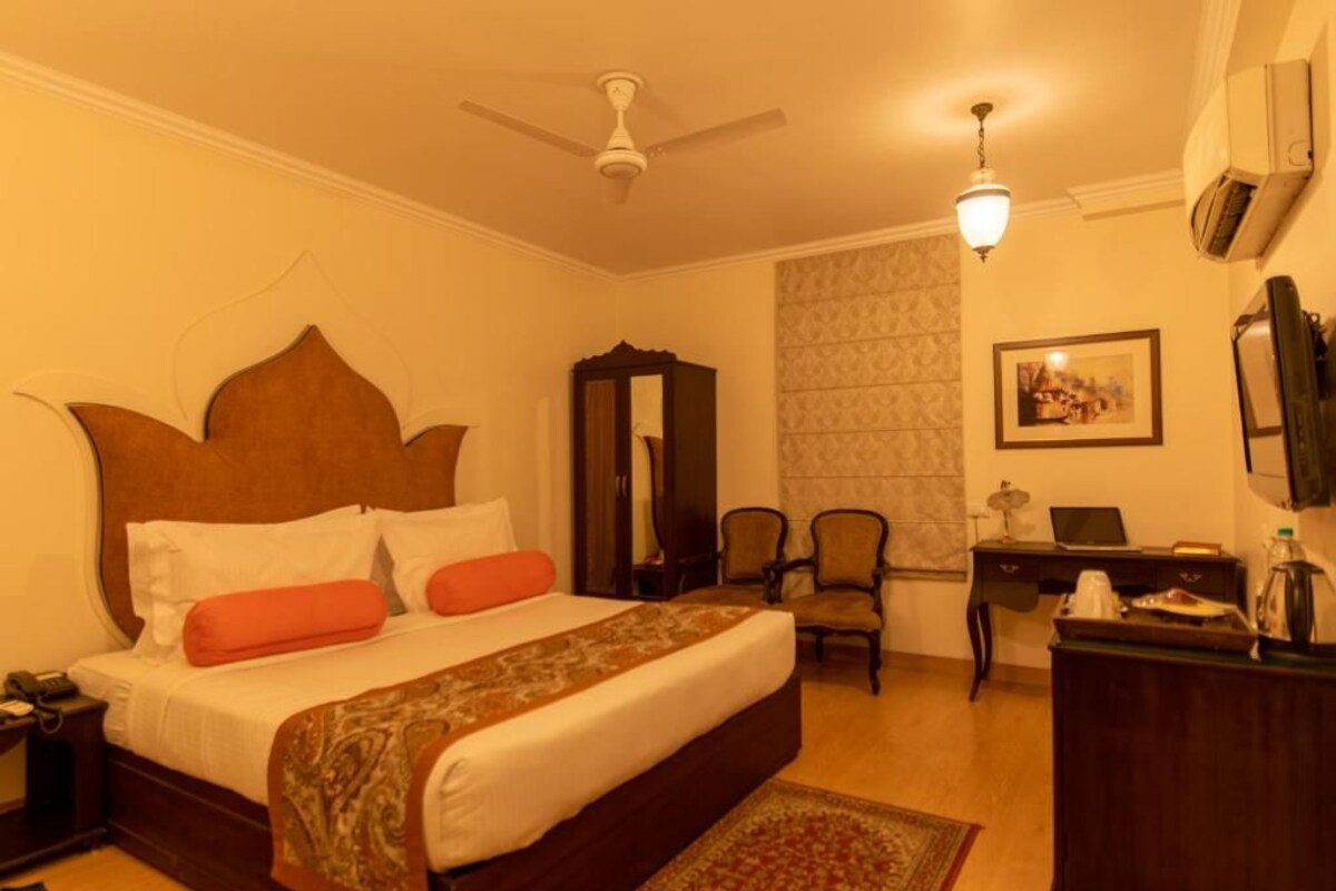 A hotel room with a bed, a desk, a chair, a ceiling fan, and a wall-mounted air conditioner.