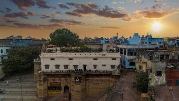 Un edificio storico con un ingresso imponente, circondato da edifici urbani fitti e un cielo al tramonto.