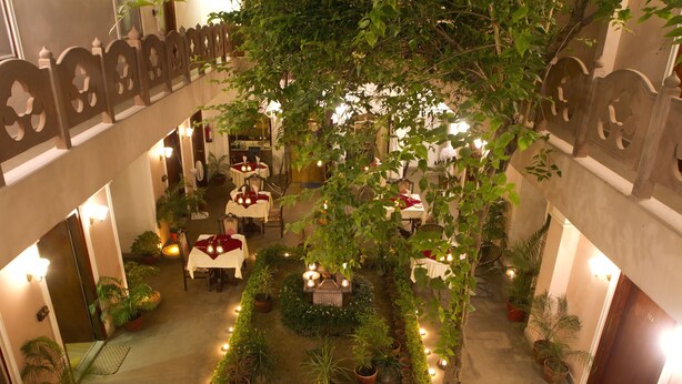 A courtyard with tables and chairs, surrounded by potted plants and a central garden area. - Amritara Suryauday Haveli (Varanasi)