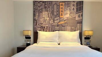A hotel room with a large bed, two bedside tables with lamps, and a wall tapestry depicting a cityscape.