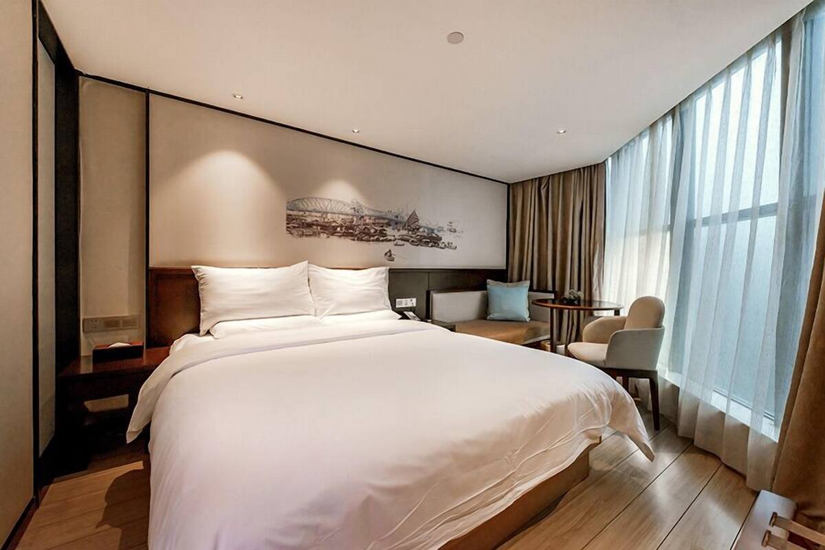 Ein modernes Hotelzimmer mit einem großen Bett, einer Sitzecke mit einem kleinen Tisch und einem großen Fenster mit Vorhängen.