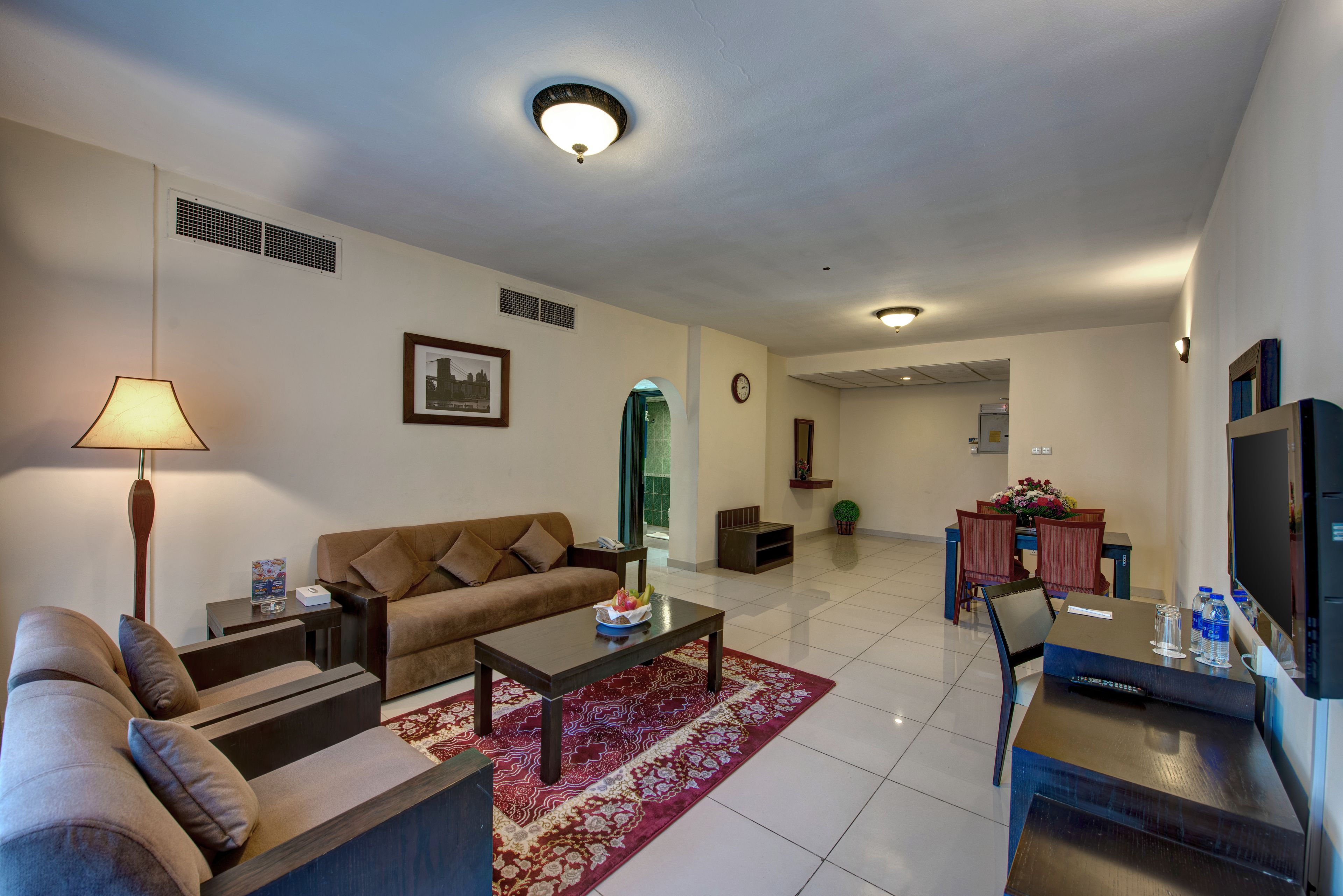 A modern living room with a sofa, coffee table, and TV. There is a dining area with a table and chairs.