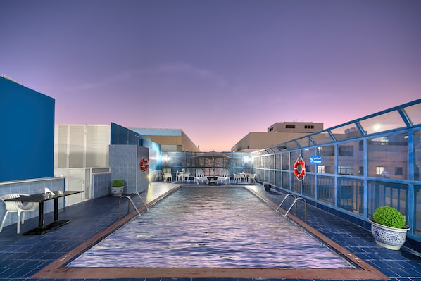 Une piscine intérieure avec un sol carrelé, un espace détente et une vue sur le paysage urbain.
