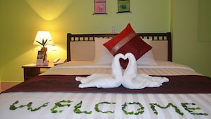 A neatly made bed with a heart-shaped towel arrangement, a red pillow, and a welcome sign made of green leaves on the bedspread. - Parklane Hotel (Siem Reap)