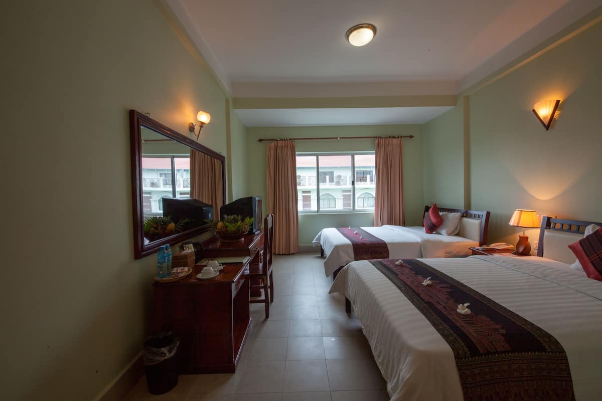 Una habitación de hotel con dos camas, un escritorio con ordenador, un espejo y una ventana con cortinas.