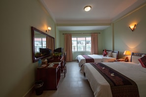 Una habitación de hotel con dos camas, un escritorio con ordenador, un espejo y una ventana con cortinas.