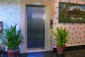 An elevator with a sign, two potted plants, and a painting on the wall. - Parklane Hotel (Siem Reap)