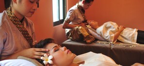 Eine Massageanwendung in einem Raum mit zwei Massagetischen, einer wird von einem Klienten und die andere von einem Therapeuten genutzt.