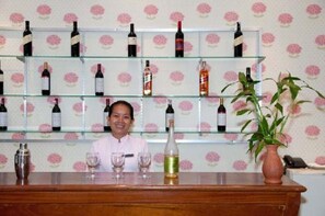 A bar area with multiple wine bottles on shelves, a potted plant, and glasses on the counter. - Parklane Hotel (Siem Reap)