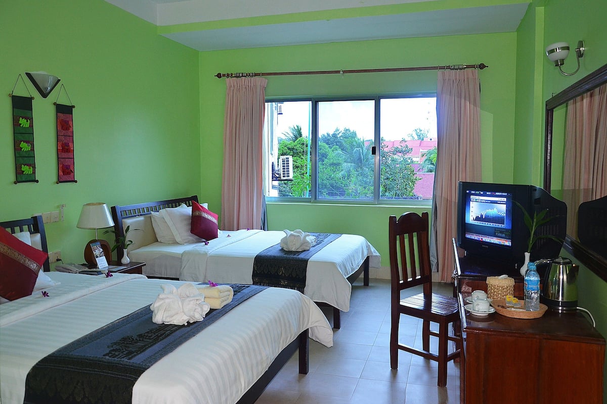 Habitación de hotel con dos camas, televisión y ventana con cortinas.