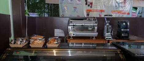 A coffee shop with a menu board, coffee machines, and a display case with pastries and dairy products.