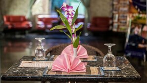 A dining table with a vase of flowers, a glass, and a folded napkin. - Parklane Hotel (Siem Reap)