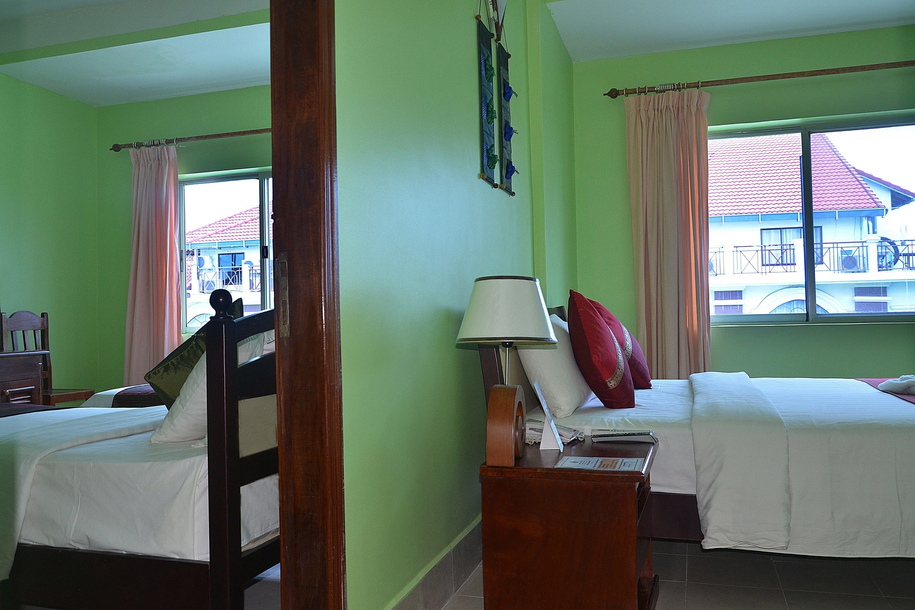A hotel room with two beds, a wooden headboard, a nightstand with a lamp, and a window with a view of a building.