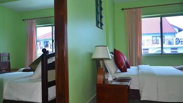 A hotel room with two beds, a wooden headboard, a nightstand with a lamp, and a window with a view of a building.