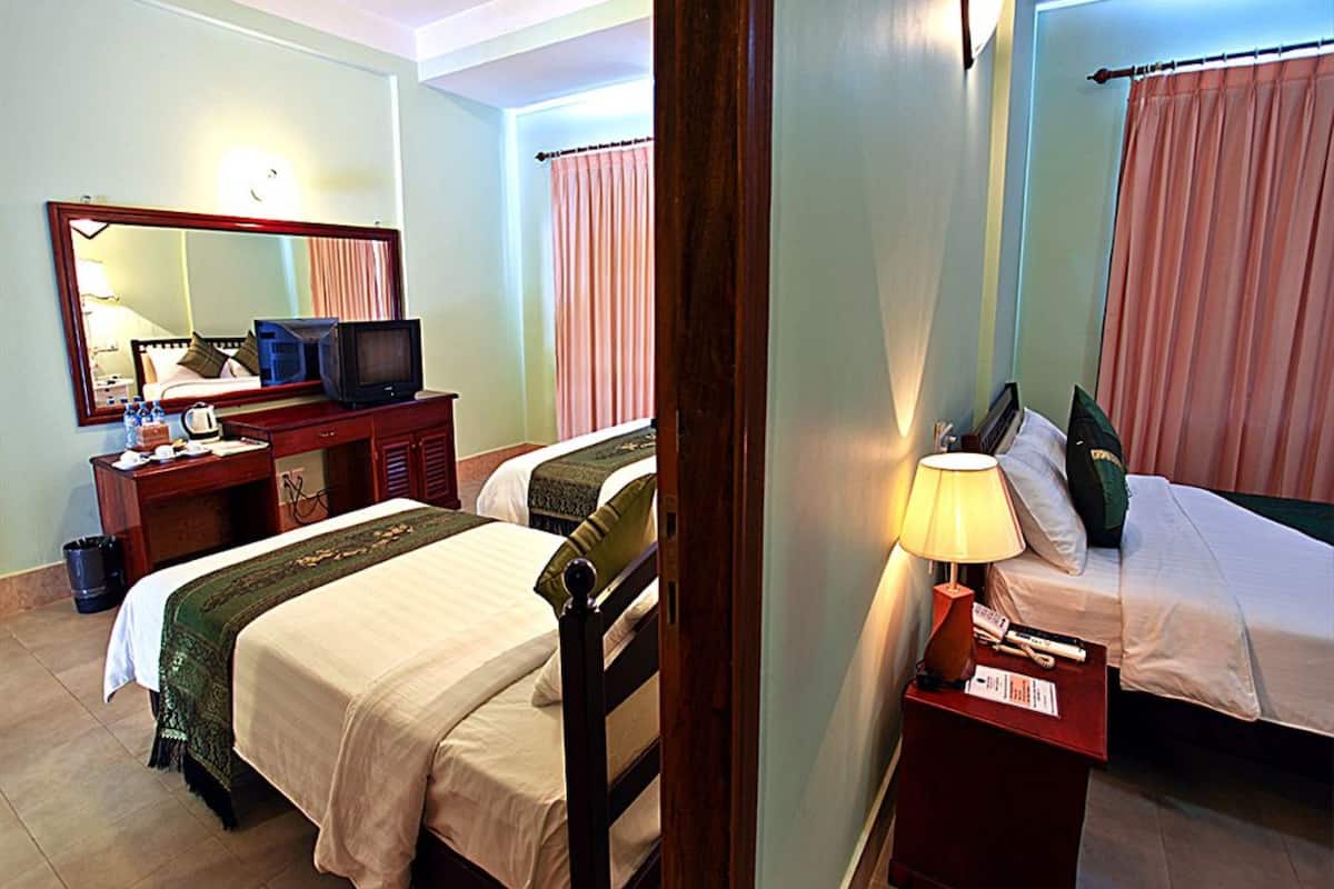 Habitación de hotel con dos camas, un escritorio, televisión, espejo y lámpara.