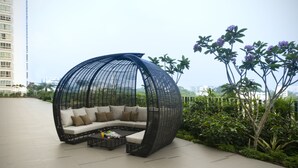 A spherical outdoor seating area with a cushioned bench and a coffee table, surrounded by greenery and overlooking a cityscape. - V Hotel Lavender (Singapore)