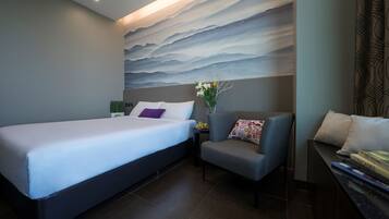 A hotel room with a bed, a small table with a vase of flowers, a chair, and a sofa.