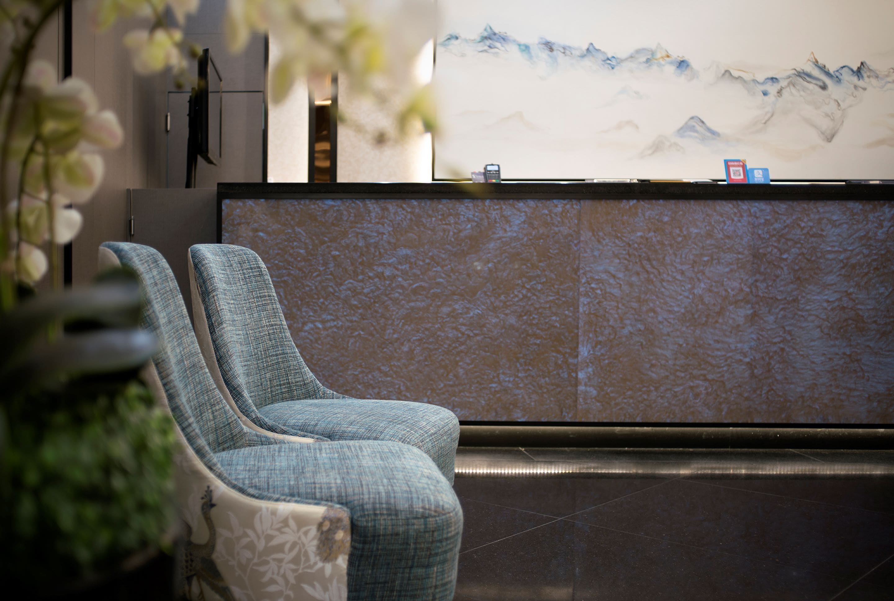 A reception area with a reception desk, two upholstered chairs, a wall-mounted phone, and a painting of mountains.