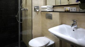 Un baño moderno con ducha envuelta en vidrio, inodoro blanco y lavamanos con espejo superior.