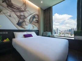Quarto de hotel moderno com uma cama grande, vista para a cidade e uma grande pintura abstrata na parede.