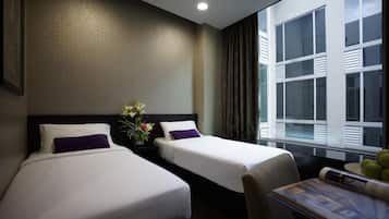 A hotel room with two beds, a nightstand with a vase of flowers, a window with curtains, and a table with a magazine.
