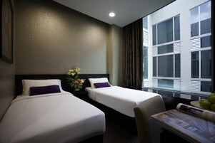 A hotel room with two beds, a nightstand with a vase of flowers, a window with curtains, and a table with a magazine.