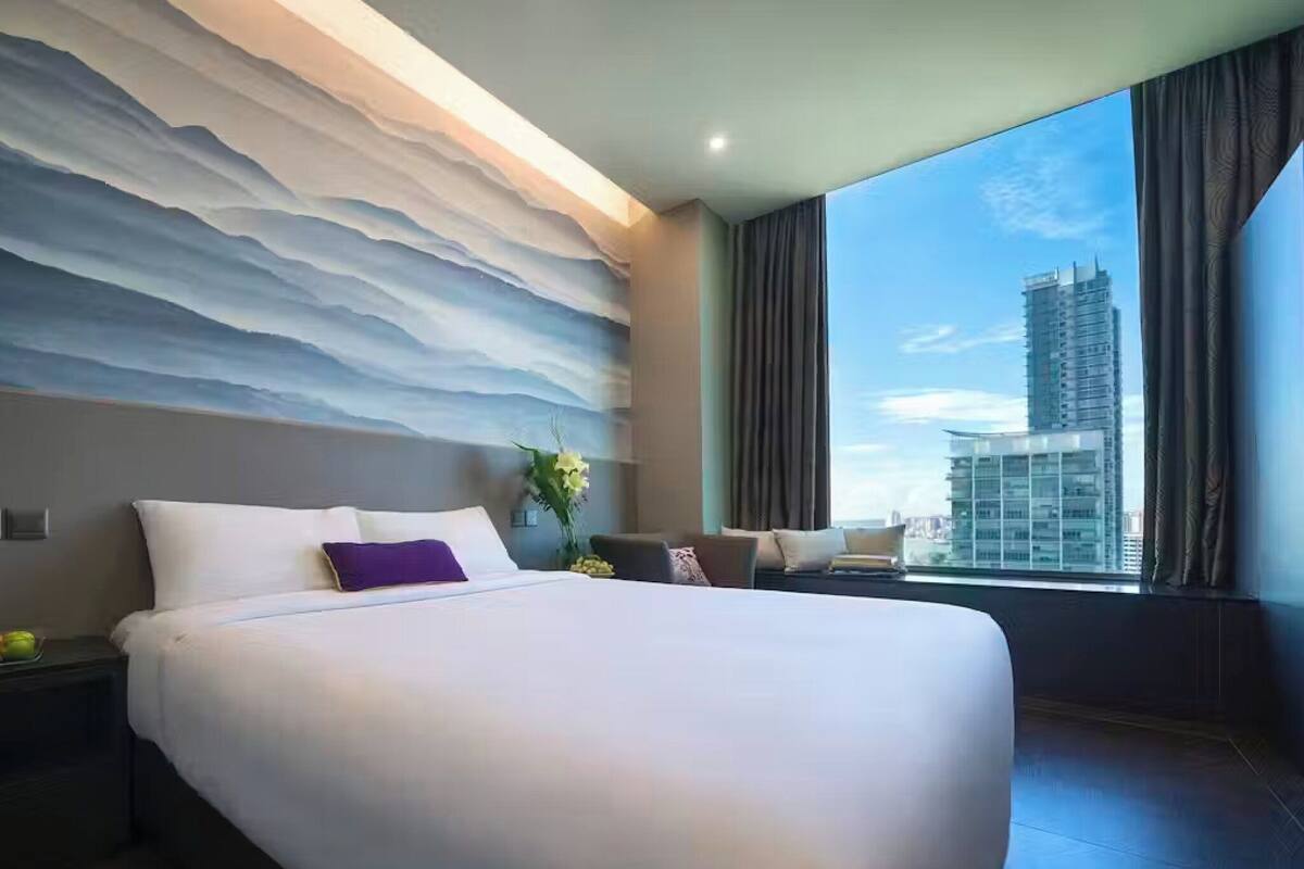 Quarto de hotel moderno com uma cama grande, vista para a paisagem urbana e parede texturizada.
