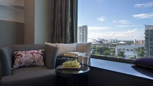 A modern living room with a sofa, a small table with a fruit plate, books, and a view of a cityscape through a window. - V Hotel Lavender (Singapore)