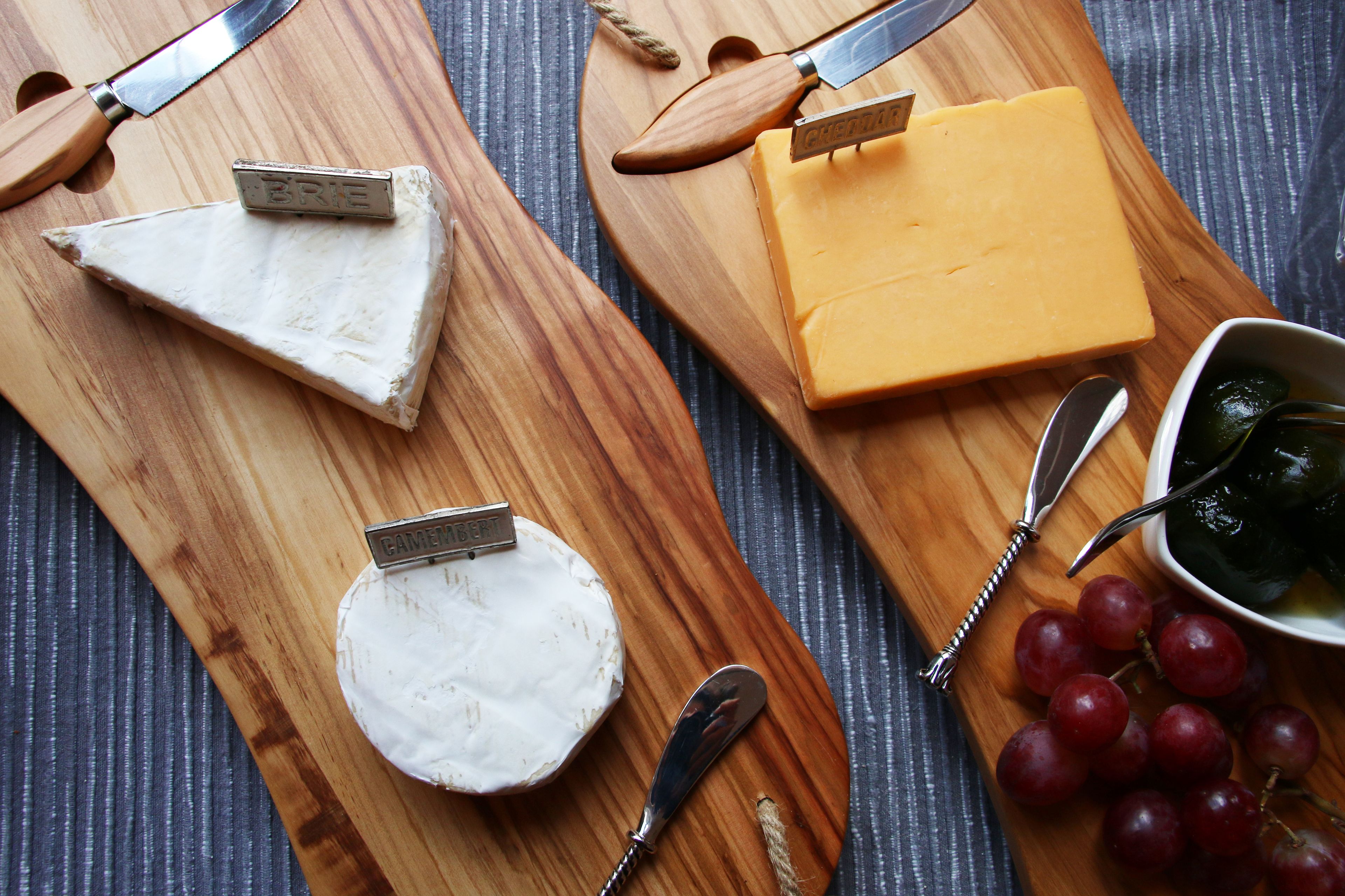 Three wooden cheese boards with different types of cheese and a bowl of grapes.
