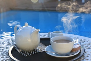 A tray with a teapot, a cup of tea, and a biscuit on a table near a pool. - Paradiso Guest House (Cape Town)