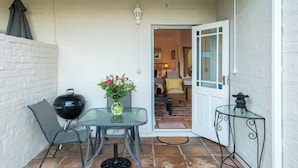 Un patio abrité avec une table, des chaises, un barbecue et un vase de fleurs.