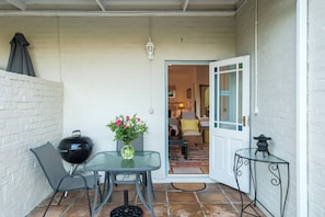 A covered patio area with a table, chairs, a grill, and a vase of flowers. - Paradiso Guest House (Cape Town)
