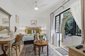 A hotel room with a bed, bedside tables, a desk, a chair, a small table with a vase, and a view of the outdoors through a large window. - Paradiso Guest House (Cape Town)